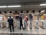 Dos agentes esperan a que una viajera acceda al Metro de Madrid para entregarle una mascarilla.