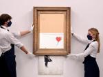 Empleados de la galería muestran la obra de Banksy 'Love is in the Bin