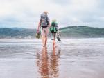 Padre e hijo caminan descalzos en la playa durante una ruta