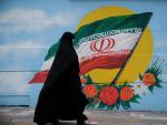 Una mujer con chador camina junto a un mural con la bandera de Ir&aacute;n en Teher&aacute;n