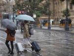 Una pareja con maletas se protegen de la lluvia bajo sus paraguas.