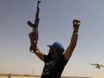 Un opositor libio, con los brazos y las armas en alto, en actitud de celebraci&oacute;n.