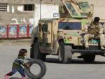 Una ni&ntilde;a juega con un neum&aacute;tico mientras dos soldados descansan en su veh&iacute;culo militar en Bagdad.