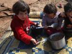 Unos ni&ntilde;os sirios comen en el suelo en un campamento de refugiados.