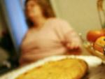 Una mujer obesa ante una mesa con varios alimentos.