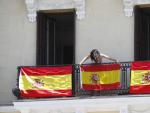 Una joven coloca banderas de Espa&ntilde;a en un balc&oacute;n de la Plaza de Oriente de Madrid.