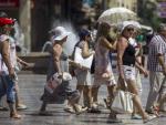 Un grupo de turistas se protegen del intenso sol con sombreros o paraguas mientras caminan por la plaza de la Virgen, en Valencia.