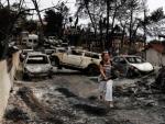 Una mujer camina entre coches calcinados en Mati (Grecia), localidad arrasada por los devastadores incendios declarados en la costa al noreste de Atenas.