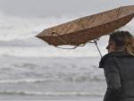 Una joven trata de protegerse de la lluvia y el viento con un paraguas en Gij&oacute;n, Asturias, en una imagen de archivo.
