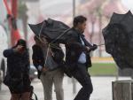 Varias personas sujetan sus paraguas intentando que no se les vuele debido al fuerte viento y a la lluvia en M&aacute;laga.