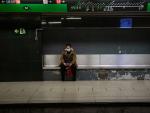 Una mujer protegida con mascarilla espera sentada en un banco del and&eacute;n a que llegue el metro, en Barcelona/Catalunya (Espa&ntilde;a) a 26 de marzo de 2020.