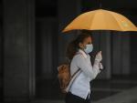 Una mujer protegida con mascarilla y guantes se resguarda de la lluvia bajo su paraguas en la quinta semana del estado de alarma por el coronavirus, Covid-19. En Sevilla (Andaluc&iacute;a, Espa&ntilde;a), a 15 de abril 2020.