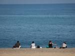 Varias personas sentadas en la Playa de la Barceloneta respetan la distancia de seguridad.