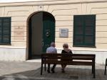 Dos personas mayores conversan sentadas en un banco y con mascarilla, ante la Residencia Geri&aacute;trica Asistida del Ayuntamiento de Mah&oacute;n en la Calle C&oacute;s de Gr&agrave;cia.