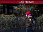 Una persona con mascarilla por el coronavirus pasa junto a un café cerrado por la pandemia, en París, Francia.