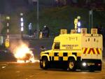 Un veh&iacute;culo policial pasa junto al mobiliario urbano quemado en los disturbios en Newtownabbey, al norte de Belfast.