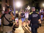 Un agente de la Guardia Urbana de Barcelona delante de personas haciendo botell&oacute;n, este s&aacute;bado.