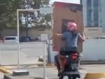 Una pareja transporta una televisión en una moto.