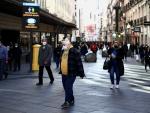 Varios viandantes pasean por el centro de Madrid, donde los carteles recuerdan el uso de la mascarilla ante las aglomeraciones.