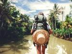 Mujer viajera con mochila parada cerca de un gran r&iacute;o tropical en un d&iacute;a soleado Una mujer viajera parada frente al r&iacute;o Kapuas en Indonesia.