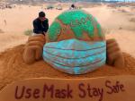 Escultura de arena del globo terr&aacute;queo con mascarilla y la palabra &quot;&oacute;micron&quot; escrita sobre el mundo.
