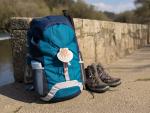 Backpack with seashell symbol of Camino de Santiago, trekking boots and poles leaning on stone wall. Pilgrimage to Santiago de Compostela. Copy space