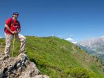 A man hiking in the Picos de Europa on the peak of Viorna near Potes, looking ahead, behind him are the high peaks and the stone cross on a cloudless summer day.