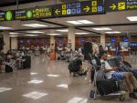 Varias personas esperan sentadas con sus maletas en el Aeropuerto Josep Tarradellas Barcelona-El Prat.