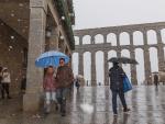 Varias personas caminan junto al acueducto mientras nieva en Segovia.