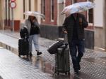 Dos personas con paraguas y maletas caminan por la calle en M&aacute;laga