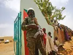 A UN peacekeeper stands guard as crowds of children and villagers gather to welcome Steven Koutsis (unseen), the United States' top envoy in Sudan, in the war-torn town of Golo in the thickly forested mountainous area of Jebel Marra in central Darfur on June 19, 2017. The town was a former rebel bastion which was recently captured by Sudanese government forces. The top US envoy in Sudan began a four-day trip to Darfur on June 18, 2017 to assess security in the war-torn region as the UN prepares to downsize its 17,000-strong peacekeeping force. His visit also comes just weeks before President Donald Trump's administration decides whether to permanently lift a two-decades old US trade embargo on Sudan. / AFP PHOTO / ASHRAF SHAZLY (Photo credit should read ASHRAF SHAZLY/AFP via Getty Images)