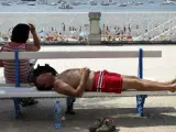 Dos personas descansan a la sombra en el paseo de la playa de La Concha de San Sebasti&aacute;n.
