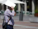 Un hombre se protege la cabeza del sol con unos papeles mientras cruza la plaza Mayor de Valladolid.