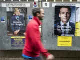 Un joven pasa junto a los carteles electorales de Le Pen y Macron.