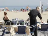 Un camarero atiende las mesas de un restaurante junto a la playa.
