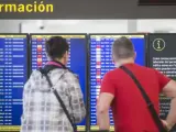 Dos viajeros observan el panel de salidas en El Prat, en el que aparecen varios vuelos cancelados a causa de una huelga de controladores franceses.
