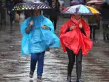Dos mujeres se protegen de la intensa lluvia, con paraguas y chubasquero, en la madrileña Puerta del Sol.
