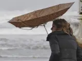 Una joven trata de protegerse de la lluvia y el viento con un paraguas en Gijón, Asturias, en una imagen de archivo.