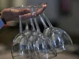 Un camarero sujeta copas de vino de cristal entre sus dedos.