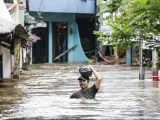 Un hombre camina con el agua prácticamente al cuello por una calle inundada en un barrio de Yakarta (Indonesia).