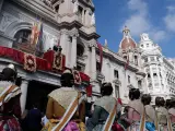 Decenas de falleras observan la bajada de la Real Senyera del balcón del Ayuntamiento de València, desde donde se inicia la procesión cívica del 9 d'Octubre