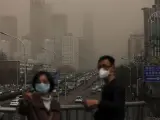 Un hombre y una mujer se protegen con máscaras de una nube de contaminación que cubre la ciudad de Pekín (China).