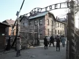 Unos visitantes del antiguo campo de concentraci&oacute;n de Auschwitz pasan bajo el famoso arco de su entrada, donde ha estado Merkel por primera vez.