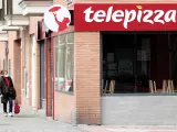 Una mujer protegida con mascarilla pasea cerca de un local de Telepizza el mismo día en el que han comenzado a servir menús para alumnos madrileños con beca comedor y así evitar que les falten alimentos por la crisis del coronavirus, en Madrid.