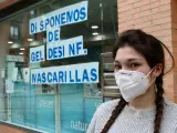 Una mujer con mascarilla ante una farmacia.