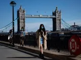Varias personas con mascarillas por la pandemia del coronavirus caminan junto al Puente de la Torre, en Londres.