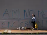 Una mujer pasea a un perro junto a una pared con una pintada, que reza &quot;a m&iacute; no me encerr&eacute;is&quot;.