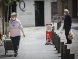 Una mujer con mascarilla, guantes y un carrito de la compra camina por la calle.