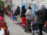 Varias personas esperan en la fila para recoger alimentos proporcionados por la Asociaci&oacute;n de vecinos de Aluche (Madrid)
