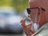 Un hombre con una mascarilla bajada fuma un cigarrillo.